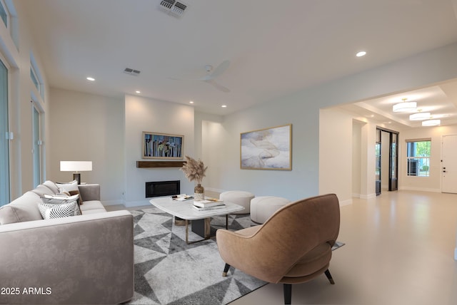 living room featuring a ceiling fan, visible vents, baseboards, a glass covered fireplace, and recessed lighting
