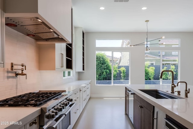 kitchen with wall chimney range hood, appliances with stainless steel finishes, a sink, light countertops, and decorative backsplash
