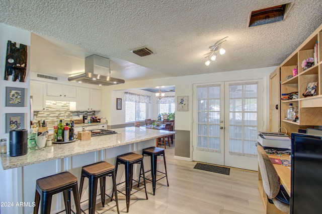 kitchen featuring extractor fan, a breakfast bar, white cabinetry, light stone countertops, and french doors