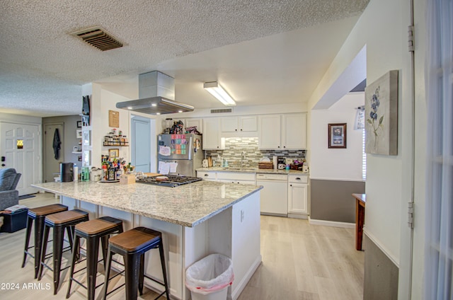 kitchen featuring white cabinets, a kitchen breakfast bar, island range hood, light hardwood / wood-style floors, and stainless steel appliances