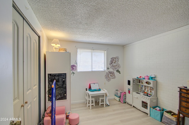 playroom featuring brick wall, a textured ceiling, and light hardwood / wood-style floors