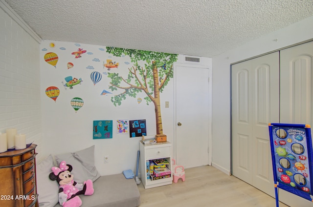 recreation room with brick wall, light hardwood / wood-style flooring, and a textured ceiling