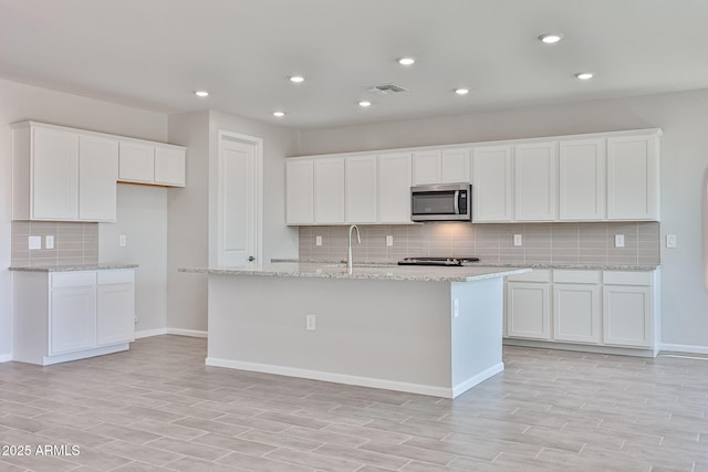 kitchen featuring visible vents, decorative backsplash, stainless steel microwave, white cabinets, and light wood-style flooring