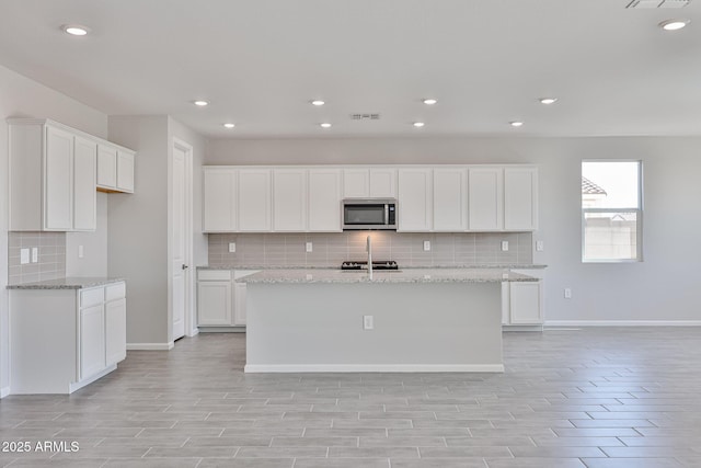 kitchen with visible vents, white cabinetry, stainless steel microwave, and tasteful backsplash
