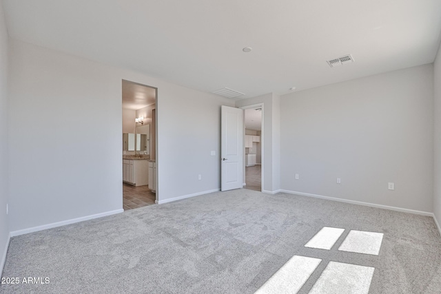 unfurnished bedroom featuring baseboards, visible vents, ensuite bathroom, and light colored carpet