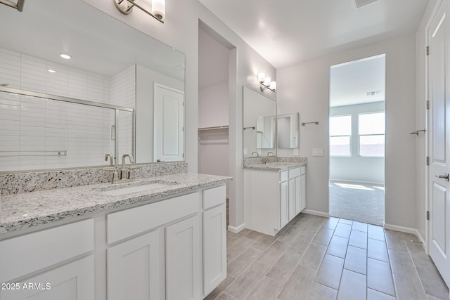 bathroom featuring baseboards, two vanities, a sink, and a stall shower