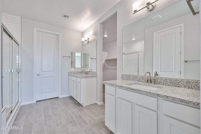 bathroom with visible vents, two vanities, a sink, and a stall shower