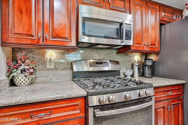 5349 W Acapulco Ln, Glendale, AZ 85306 - kitchen with appliances with stainless steel finishes, backsplash, brown cabinetry, and light stone countertops