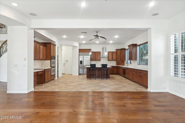 kitchen with a kitchen island, appliances with stainless steel finishes, pendant lighting, light hardwood / wood-style floors, and wall chimney exhaust hood