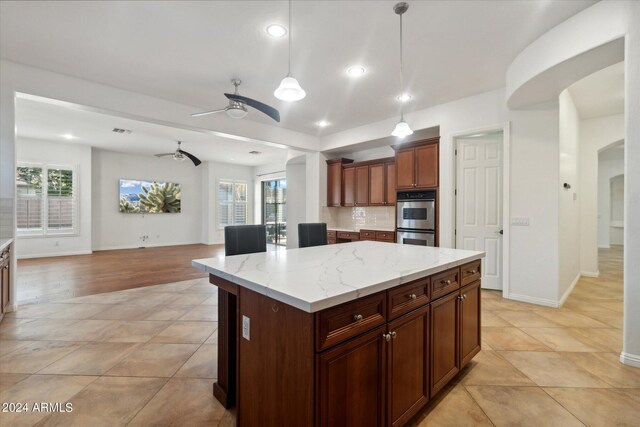 kitchen featuring a kitchen island, pendant lighting, ceiling fan, light stone counters, and stainless steel double oven