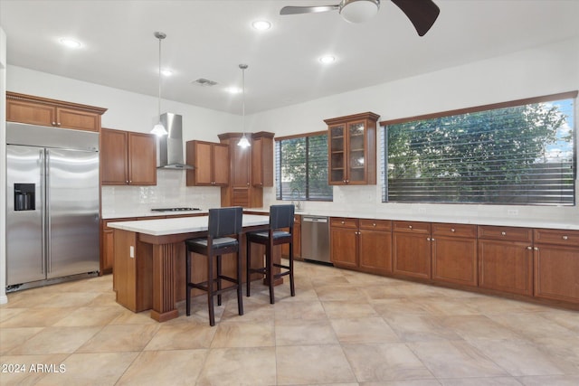 kitchen featuring a kitchen island, a breakfast bar area, hanging light fixtures, stainless steel appliances, and wall chimney range hood