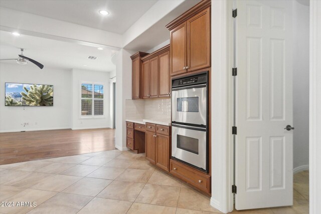 kitchen with double oven, light tile patterned floors, built in desk, and backsplash