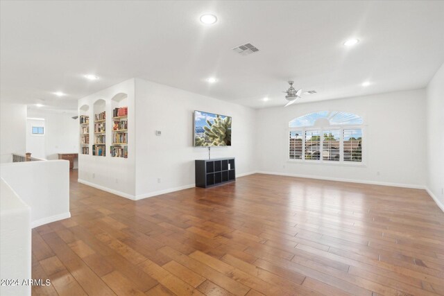 unfurnished living room with wood-type flooring, ceiling fan, and built in shelves