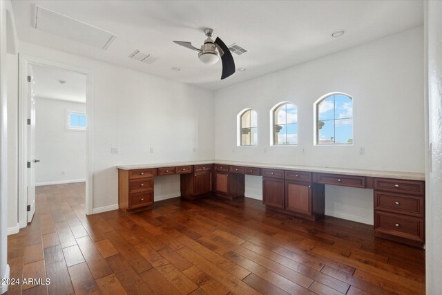 unfurnished office featuring a wealth of natural light, built in desk, and dark hardwood / wood-style flooring