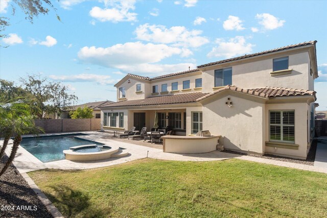 rear view of property featuring a swimming pool with hot tub, a lawn, and a patio