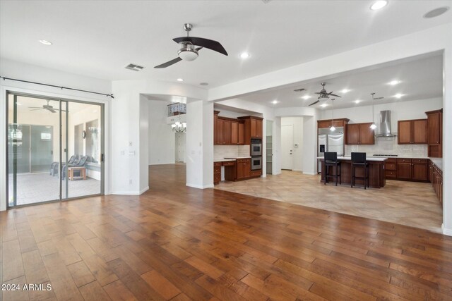 unfurnished living room with ceiling fan with notable chandelier and light hardwood / wood-style flooring