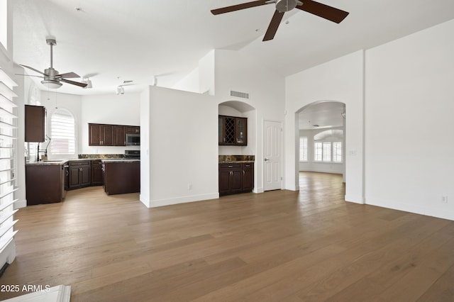 18873 N 94th Way, Scottsdale, AZ 85255 - unfurnished living room featuring a ceiling fan, arched walkways, healthy amount of natural light, light wood-style floors, and a high ceiling
