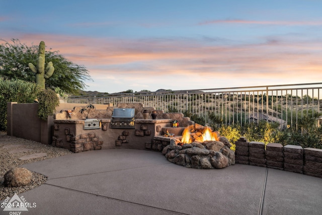 patio terrace at dusk featuring an outdoor kitchen, area for grilling, and an outdoor fire pit