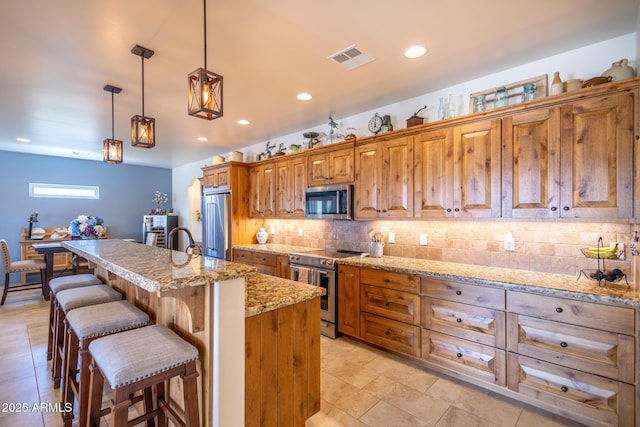 965 Calle Azul, Wickenburg, AZ 85390 - kitchen featuring stainless steel appliances, brown cabinets, decorative backsplash, a kitchen bar, and a center island with sink