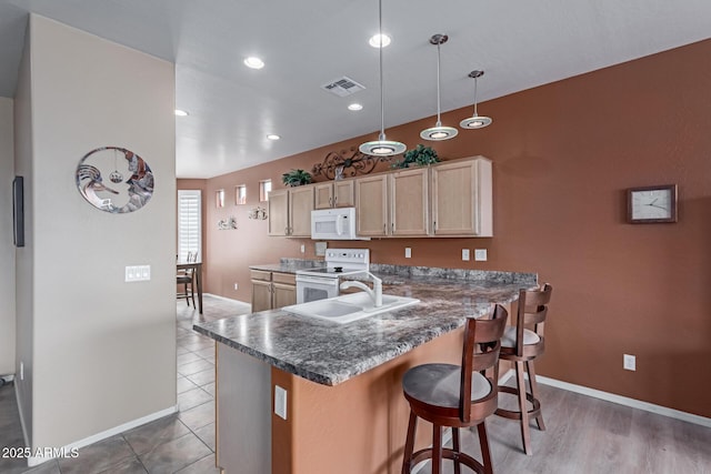 kitchen featuring white appliances, visible vents, a breakfast bar area, a peninsula, and a sink