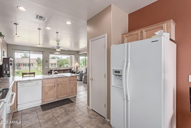 kitchen featuring visible vents, light brown cabinetry, open floor plan, a sink, and white appliances