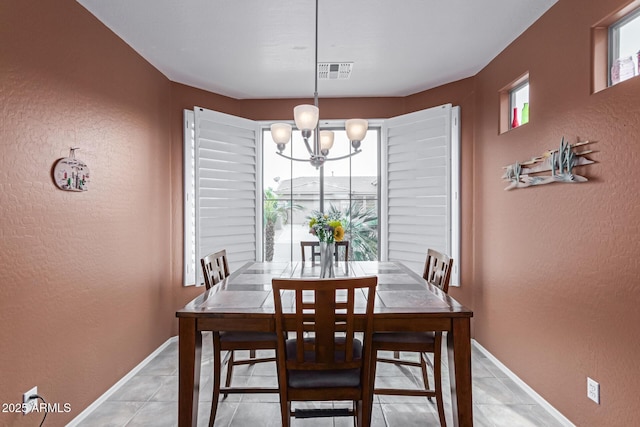 dining room with light tile patterned floors, visible vents, a textured wall, an inviting chandelier, and baseboards