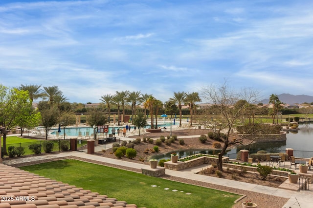 view of property's community with a lawn, a water view, fence, and a pool