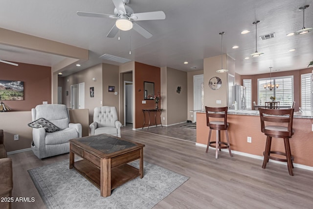 living area with light wood-style floors, visible vents, baseboards, and ceiling fan with notable chandelier