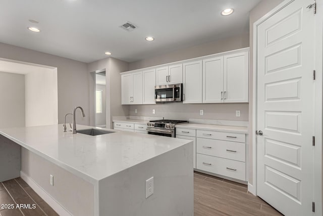 kitchen featuring white cabinetry, stainless steel appliances, a kitchen island with sink, light stone counters, and sink