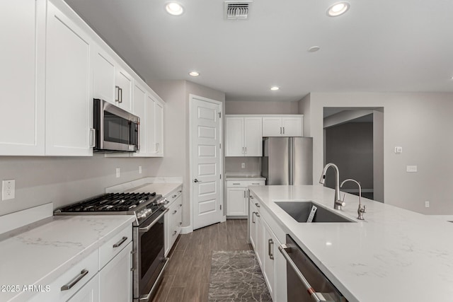 kitchen with light stone countertops, stainless steel appliances, white cabinetry, and sink