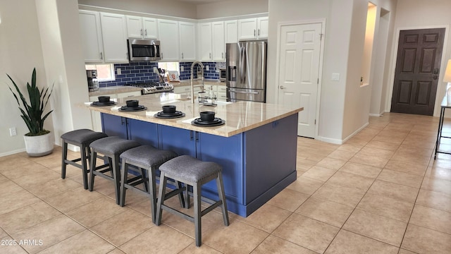 kitchen featuring light tile patterned floors, stainless steel appliances, tasteful backsplash, and white cabinetry