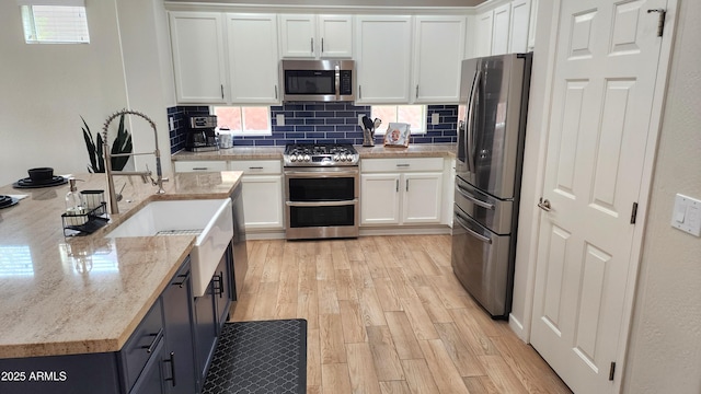 kitchen featuring light wood-type flooring, backsplash, white cabinetry, stainless steel appliances, and light stone countertops