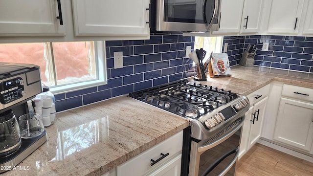 kitchen featuring light wood finished floors, light stone counters, decorative backsplash, white cabinets, and stainless steel appliances