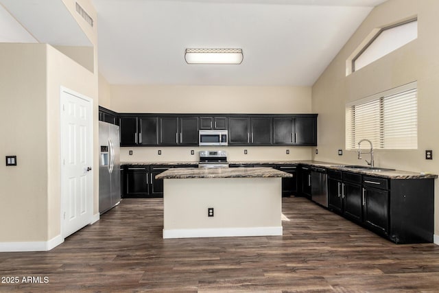 kitchen featuring appliances with stainless steel finishes, light stone countertops, a center island, dark hardwood / wood-style flooring, and sink