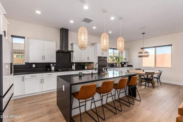 kitchen featuring black gas cooktop, white cabinets, wall chimney exhaust hood, an island with sink, and a healthy amount of sunlight