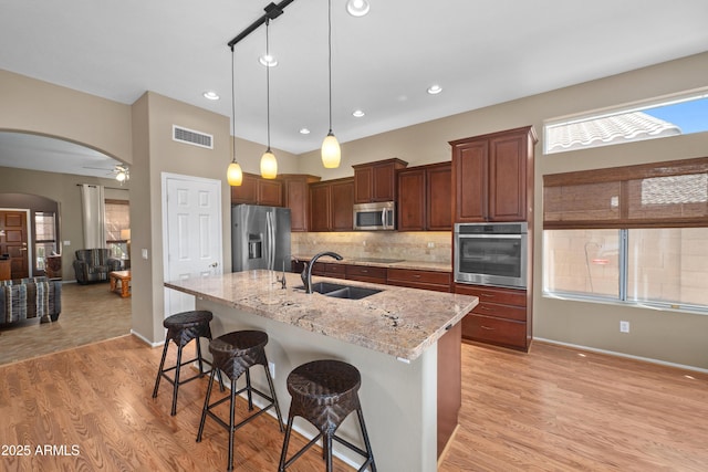 11553 W Cottontail Ct, Surprise, AZ 85378 - kitchen with appliances with stainless steel finishes, a sink, arched walkways, light wood-type flooring, and a kitchen breakfast bar