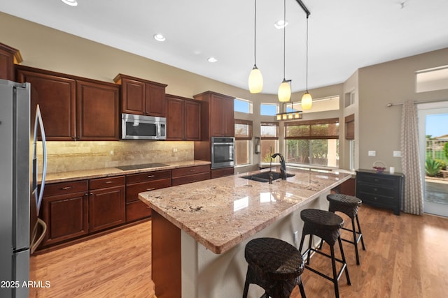 11553 W Cottontail Ct, Surprise, AZ 85378 - kitchen featuring appliances with stainless steel finishes, a sink, light wood-style floors, backsplash, and a kitchen breakfast bar
