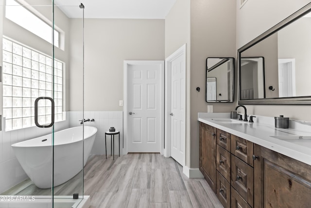 8848 E Conquistadores Dr, Scottsdale, AZ 85255 - bathroom featuring double vanity, a freestanding bath, tile walls, wainscoting, and wood finished floors