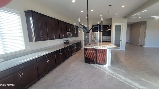 kitchen with appliances with stainless steel finishes, dark brown cabinets, a kitchen island with sink, sink, and pendant lighting