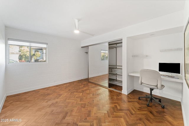 home office with parquet flooring, brick wall, and a healthy amount of sunlight