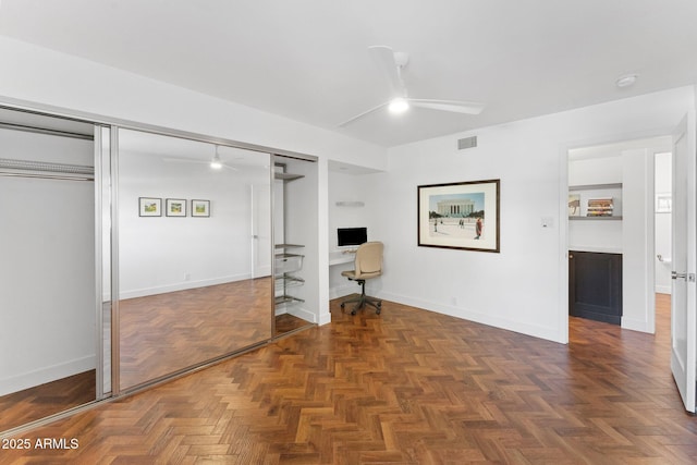 unfurnished bedroom featuring built in desk, dark parquet floors, a closet, and ceiling fan