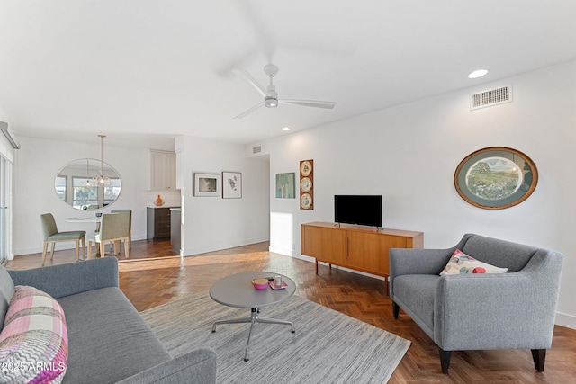 living room with dark parquet flooring and ceiling fan with notable chandelier