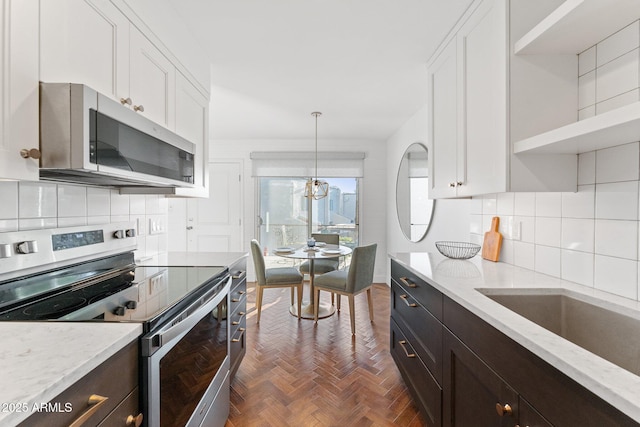 kitchen with appliances with stainless steel finishes, dark parquet floors, white cabinetry, hanging light fixtures, and light stone countertops