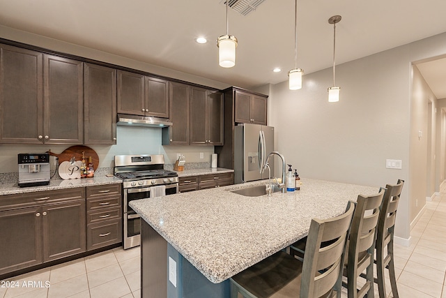 kitchen featuring light stone countertops, pendant lighting, a breakfast bar area, a center island with sink, and appliances with stainless steel finishes