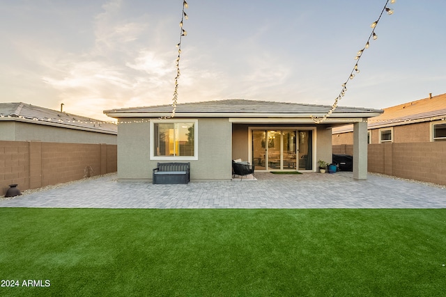 back house at dusk featuring a lawn and a patio area