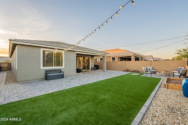 back house at dusk with a lawn, a patio area, and an outdoor fire pit