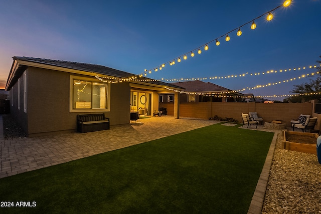 back house at dusk with a yard and a patio