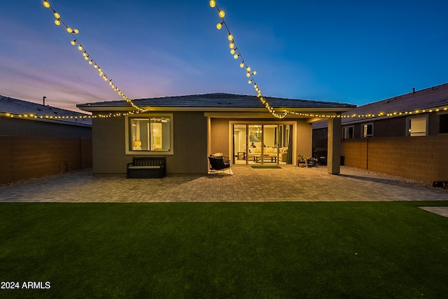 back house at dusk featuring a yard and a patio