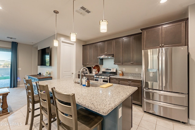 kitchen featuring sink, stainless steel appliances, light stone counters, decorative light fixtures, and a kitchen island with sink