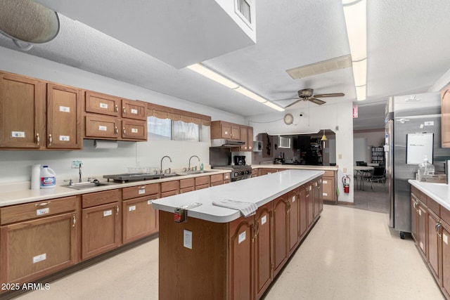 kitchen with ceiling fan, sink, black range, a kitchen island, and stainless steel refrigerator